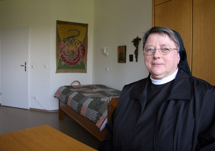 Schwester Magdalena in Ordenstracht in ihrem Zimmer, hinter ihr das Bett, ein bemaltes Wandtuch und eine Ikone